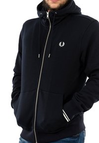 Felpa con zip color navy realizzata in misto cotone. Presenta un logo bianco sul petto, polsini a coste con strisce bianche e ampie tasche frontali.