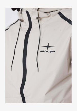 Giubbotto beige con dettagli neri, dotato di collo a imbuto, zip frontale, lacci regolabili e logo sul petto.