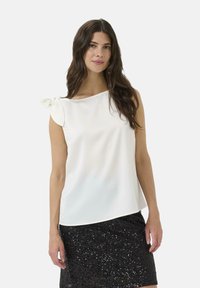 Top sans manches blanc avec un détail de nœud sur l'épaule gauche, fabriqué en tissu lisse, associé à une jupe en sequins noirs.