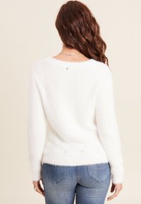 Maglione bianco soffice con maniche lunghe, scollatura rotonda e dettagli a punto orlato all'orlo. Abbinato a jeans blu chiaro.