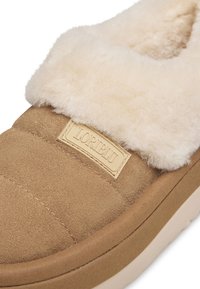 Scarpa slip-on in suede tan con colletto soffice di colore crema, dotata di un marchio beige e di una suola testurizzata e imbottita.