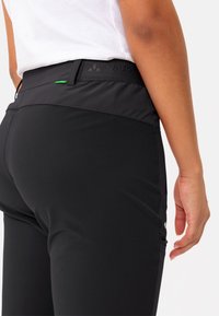 Zwarte athletische broek met een nauwsluitend ontwerp, elastische tailleband en een subtiele textuur. Kenmerkt een groene accent en branding op de taille.