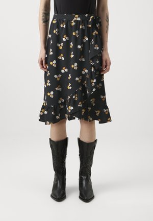 Schulterfreier schwarzer Rock mit floralem Muster und Rüschensaum, der gelbe und weiße Blumen zeigt. Kombiniert mit schwarzen Cowboy-Stiefeln mit filigranen Designelementen.