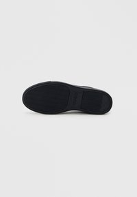 Black sneaker sole with textured pattern, featuring an embossed logo that reads "HUGO." Rounded toe and minimalistic design elements.