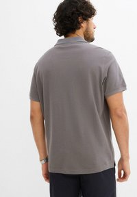Polo shirt in cotone grigio con maniche corte, colletto piatto e spacchi laterali all'orlo. Design semplice senza motivi o accenti notevoli.