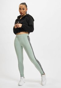 Kuttet svart hettegenser med frynset kant, sammen med myntegrønne leggings med sidestriper og svarte detaljer. Hvite joggesko fullfører antrekket.