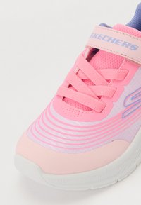La chaussure de sport rose présente un upper texturé, un design superposé, des lacets élastiques et une sangle en Velcro, avec une semelle blanche et de subtiles accents bleus.