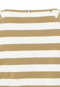 Gros plan sur un tissu rayé horizontal beige et blanc, montrant l'encolure et les détails de couture d'un vêtement textile.