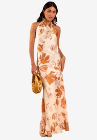 Halternekk bloemen jurk in crème met oranje en roze bloemenpatroon, vloeiende ontwerp, gemaakt van soepele stof, gecombineerd met een gouden clutch.