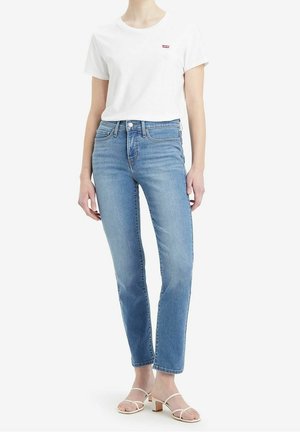 Camiseta blanca de algodón con un pequeño logo rojo, combinada con unos jeans de mezclilla azul claro de corte recto y detalles sutiles de desgaste.