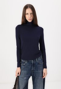 Navy langermet genser med høye krage i mykt materiale, satt sammen med løse, falmede blå jeans. Outfiten har en avslappet passform og uformell design.