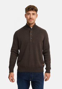 Mørkebrun, strikket sweater med høj krave, tre-knaps lukning, ribbede manchetter og kant. Har en struktureret finish og et lille logo mærke.
