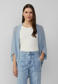 Lichtblauwe, opengehaakte cardigan met een ontspannen fit, voorzien van brede mouwen. Gedragen over een wit t-shirt en blauwe high-waisted jeans.