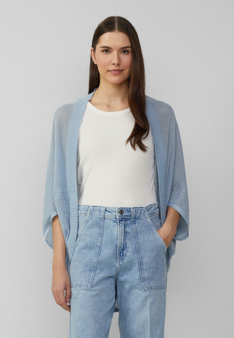Lichtblauwe, opengehaakte cardigan met een ontspannen fit, voorzien van brede mouwen. Gedragen over een wit t-shirt en blauwe high-waisted jeans.