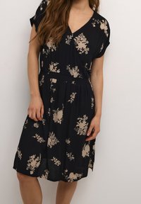 Lichtgewicht jurk met bloemenprint. Donker marineblauwe achtergrond met beige bloemmotieven. V-halslijn en korte mouwen, smalle taille.