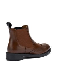 Stivale Chelsea in pelle marrone con pannelli laterali elasticizzati, dettagli in brogue e suola in gomma nera. Presenta una linguetta per facilitare l'indossamento.
