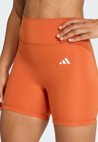 Oranžové elastické šortky s vysokým pásom, s bielym logom Adidas. Hladká textúra a priliehavý strih vhodný na aktívne nosenie.