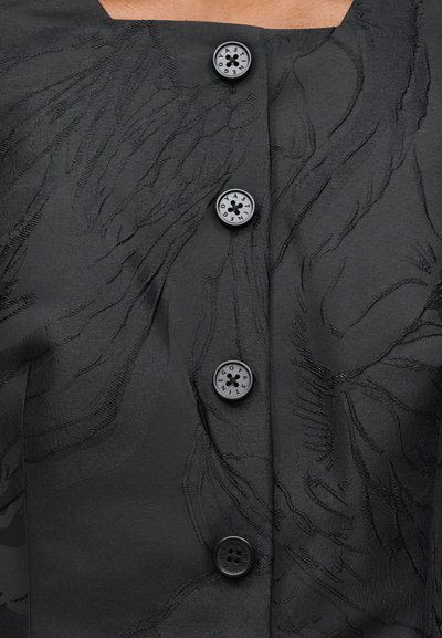 Μαύρο υφασμάτινο ύφασμα με υφή και ανθικό σχέδιο με τέσσερα μαύρα κουμπιά, τρία από τα οποία εμφανίζουν γράμματα σε κυκλική διάταξη.