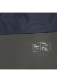 L'etichetta su tessuto scuro riporta: Serie URBAN ECO, Numero di Modello OCL01007.006, Materiale Tessuto Riciclato, Coordinate di Origine Design 47°19'32.02"N 12°47'39.98"E.