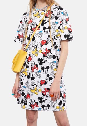 Woman wearing white dress patterned with colorful Mickey Mouse, Minnie Mouse, Donald Duck, and Pluto faces, carrying yellow crossbody bag.