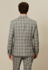 Blazer de cuadro gris con un corte estructurado, solapas con muesca y botones negros, combinado con pantalones a juego, con tejido texturizado visible.