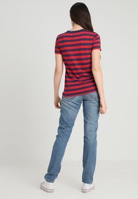 Camiseta de rayas rojas y marinas de algodón, combinada con unos vaqueros rectos de color azul claro y zapatillas blancas, mostrando un atuendo casual visto desde atrás.