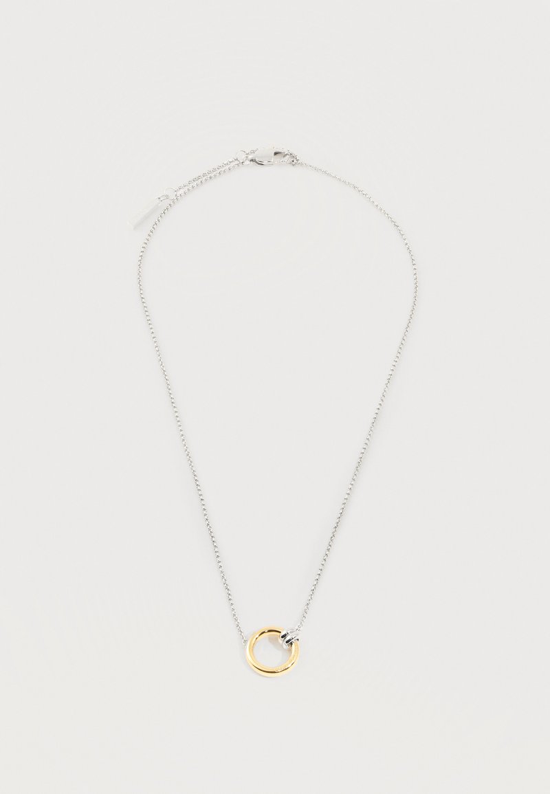 Collier chaîne en argent avec un petit pendentif anneau en or et une fermeture à fermoir argenté sur fond blanc.