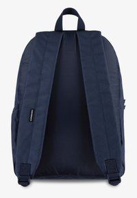 Un sac à dos bleu marine en tissu texturé, doté de bretelles réglables, d'une poignée supérieure et d'un accent logo. L'intérieur est spacieux et non structuré.