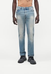 Vaqueros de mezclilla azul claro con corte recto, acabado desgastado y diseño tradicional de cinco bolsillos. Combinados con zapatillas negras.