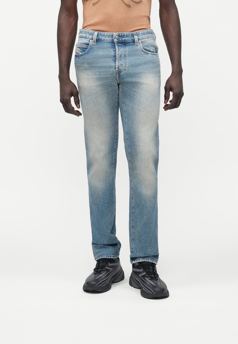 Vaqueros de mezclilla azul claro con corte recto, acabado desgastado y diseño tradicional de cinco bolsillos. Combinados con zapatillas negras.