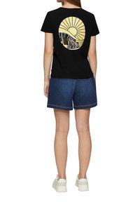 Zwart t-shirt met korte mouwen met een zonnenafbeelding in geel en tekst. Gepaarde met blauwe denim shorts en witte sneakers. Eenvoudig ontwerp.