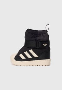 Botte d'hiver Adidas noire et beige avec trois bandes, sangle velcro, languette et semelle épaisse texturée, vue en profil gauche.