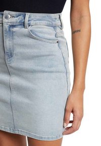 Jupe en denim bleu clair avec un design ajusté, poches avant et taille visible. Dotée d'une fermeture éclair et d'un bouton en haut.