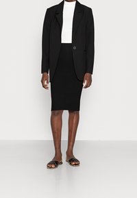 Blazer noir sur un haut blanc, associé à une jupe crayon noire à côtes et des sandales ouvertes noires à talons avec une sangle texturée.