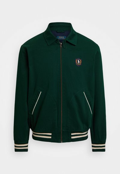 Veste zippée verte avec un col pointu, des accents de rayures blanches et un patch logo sur le côté gauche de la poitrine. Comprend deux poches avant.