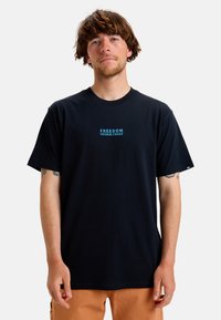 Svart t-shirt med kort ärm gjord av bomull, med en liten blå textlogga "FREEDOM FROM CHAOS" på bröstet. Klassisk passform, rund hals.