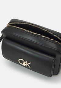 Černá kožená taška se zlatým zipem a kovovým logem. Obsahuje hlavní přihrádku a přední kapsu, která vystavuje hladký povrch.