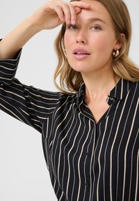 Camicia nera con righe beige verticali, design con bottoni, colletto e maniche lunghe. Texture liscia con una silhouette aderente.