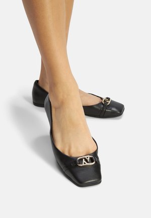 Czarne baleriny z licowej skóry z kwadratowym noskiem, z ozdobą w postaci złotego akcentu z przodu oraz niskim, zaokrąglonym obcasem.