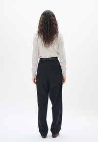 Maglione grigio a maniche lunghe abbinato a pantaloni neri a vita alta e larghi. Visibili riccioli testurizzati e scarpe a fantasia.
