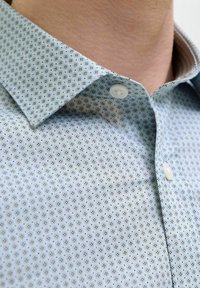 Camicia azzurro chiaro con motivo, dotata di colletto button-down, caratterizzata da piccoli disegni geometrici e due bottoni bianchi all'escursione del collo.