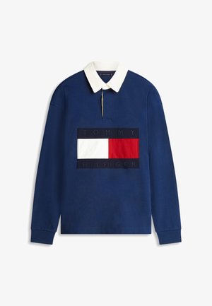 Polo de manga larga azul marino con cuello blanco y gran parche con el logo de Tommy Hilfiger en rojo, blanco y azul marino en el pecho.