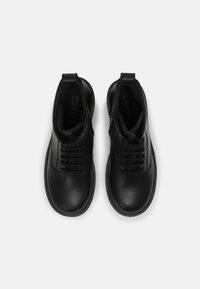 Botas altas de cuero negro con una textura suave, que cuentan con un diseño de cordones y cremalleras laterales para facilitar su uso. Suela y costuras en negro a juego.
