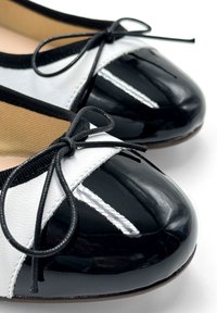 Ballet flat bicolor in bianco e nero con punta in pelle verniciata, tomaia in pelle, dettaglio a fiocco e cucitura bianca a contrasto lungo la cucitura.