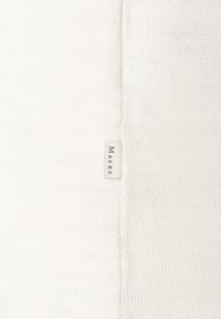 Hellbeige Strickpullover mit weicher Textur. Verfügt über eine Seitennäht und ein gewebtes Etikett mit der Aufschrift "MAERZ" in einer minimalistischen Schriftart.