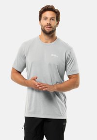T-shirt grigio chiaro a maniche corte realizzato in tessuto morbido, con un piccolo logo sul petto sinistro, abbinato a pantaloni neri.