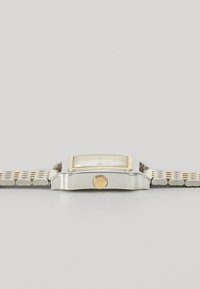 Montre en argent et en or avec un cadran rectangulaire, un bracelet texturé et une couronne hexagonale, présentant un cadran transparent et un design minimaliste.