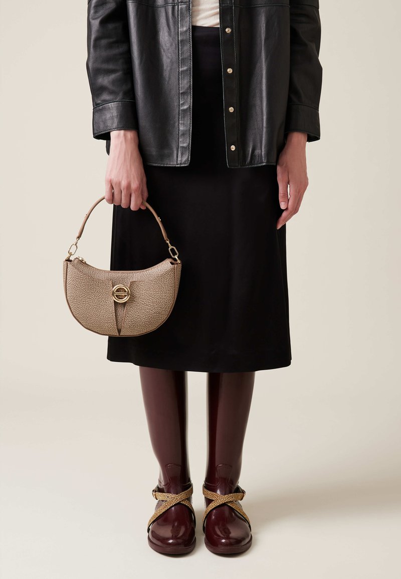Beige structured handbag with circular gold accent, worn with a black skirt and leather jacket, paired with maroon shoes and burgundy tights.
