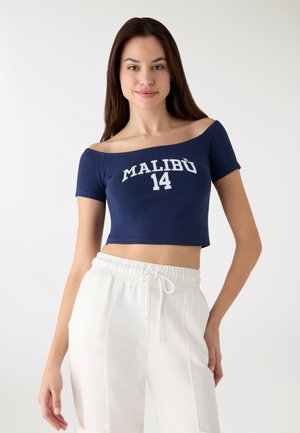 Top corto navy a maniche corte con stampa bianca "MALIBU 14". Abbinato a pantaloni bianchi a vita con coulisse e vestibilità comoda. Tessuto dalla texture liscia.