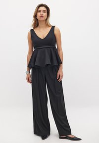 Čierny peplum top s výstrihom do V a širokými nohavicami z hladkej tkaniny. Má rozšírený lem a elegantný strih, doplnený o špičaté balerínky.